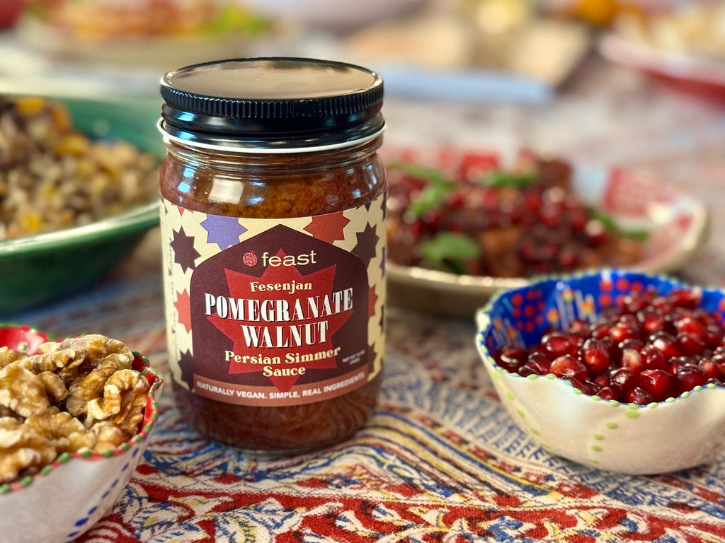 Jar of Fesenjan Pomegranate Walnut Persian Simmer Sauce on a table with bowls of ingredients.