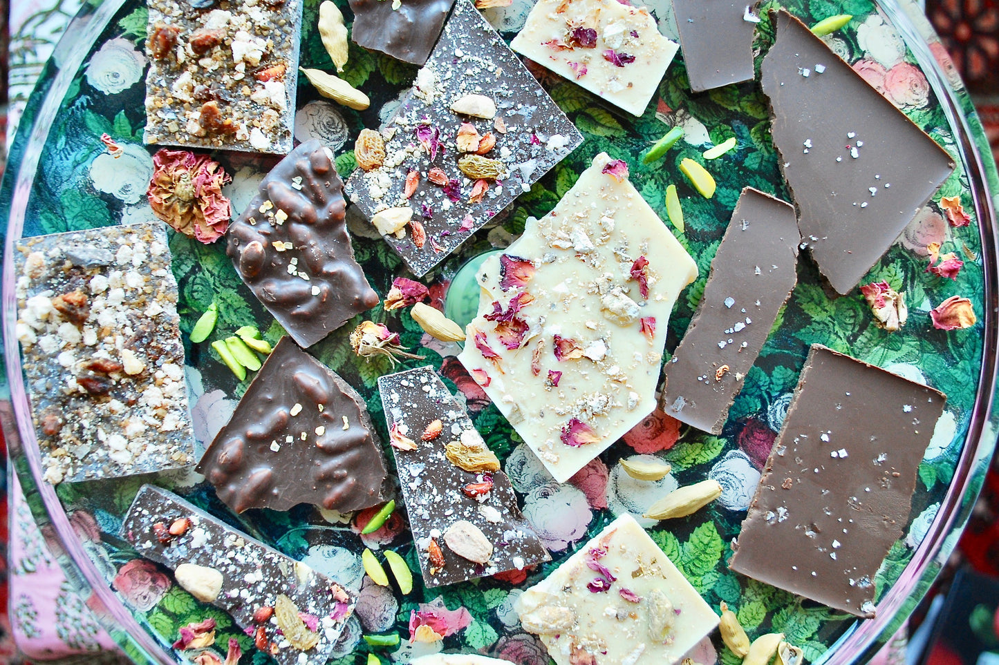 A selection of handcrafted chocolate bars with various toppings and inclusions, including nuts and spices, displayed on a glass plate.