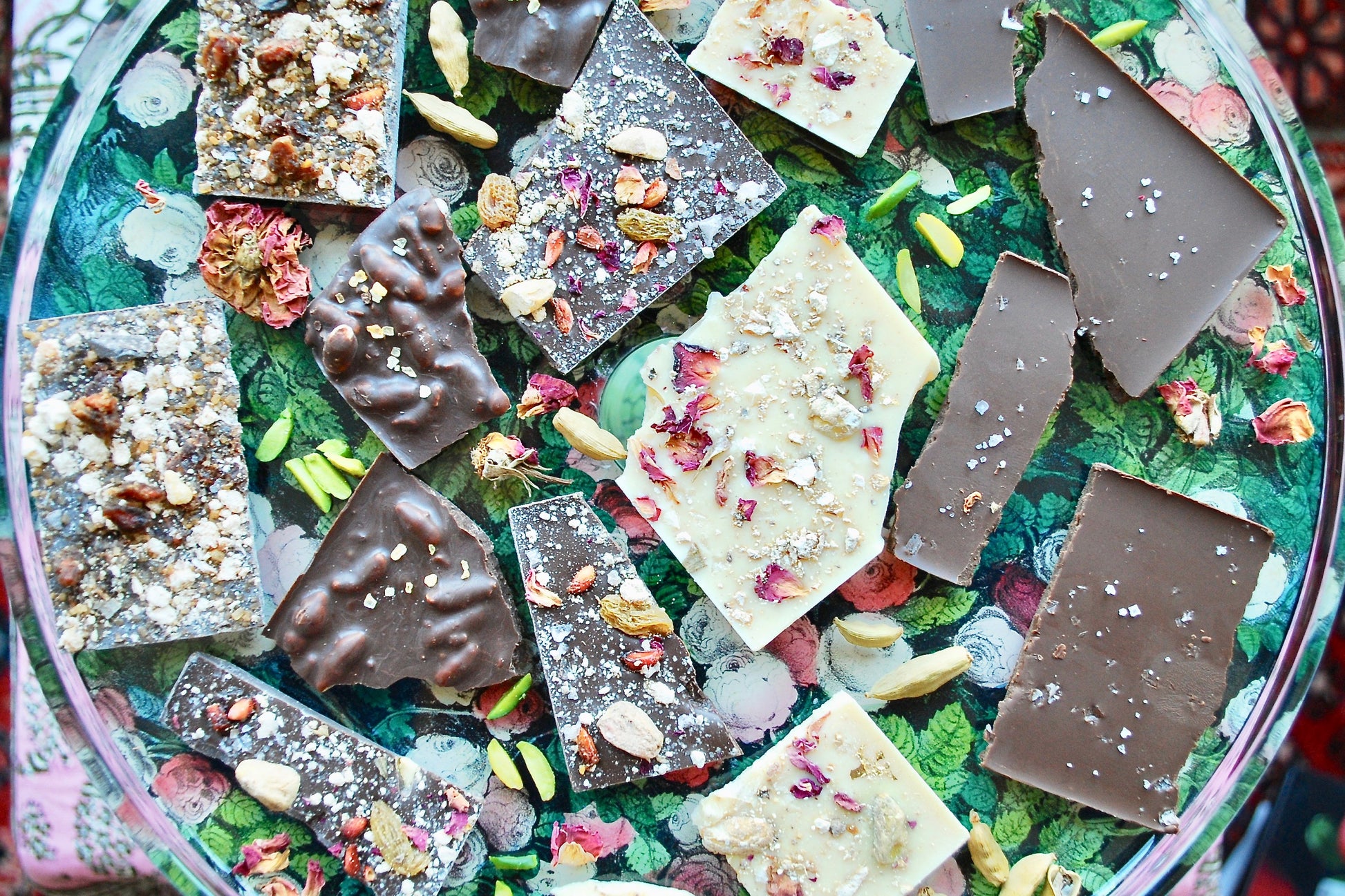 A selection of handcrafted chocolate bars with various toppings and inclusions, including nuts and spices, displayed on a glass plate.