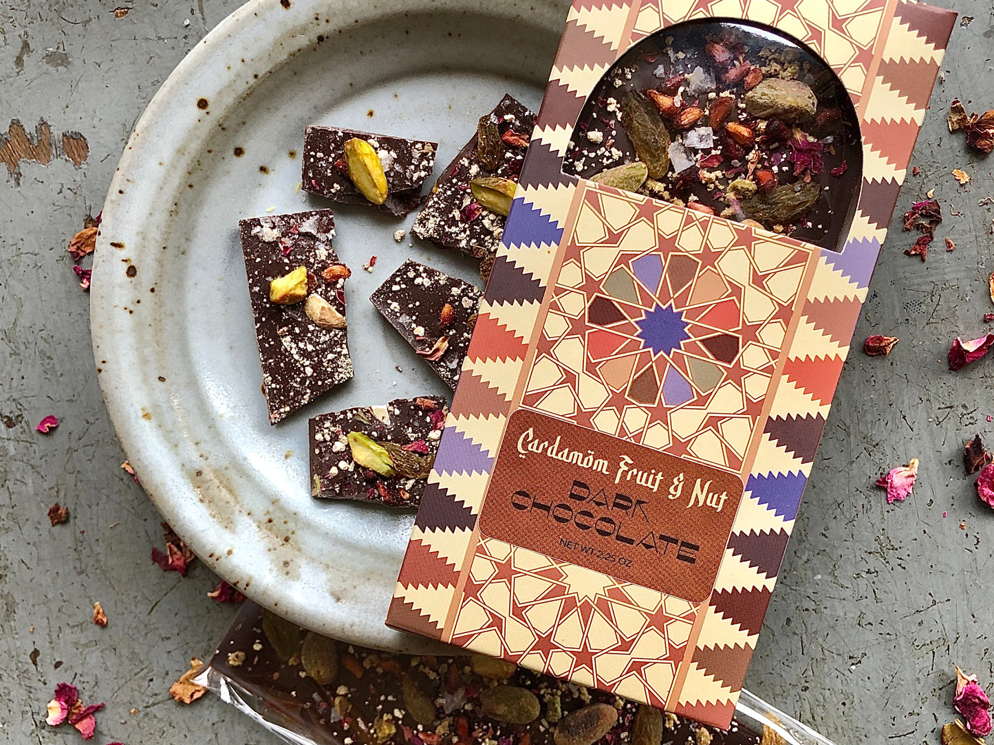 Cardamom Fruit and Nut Dark Chocolate Bar on a plate with pieces of chocolate beneath it