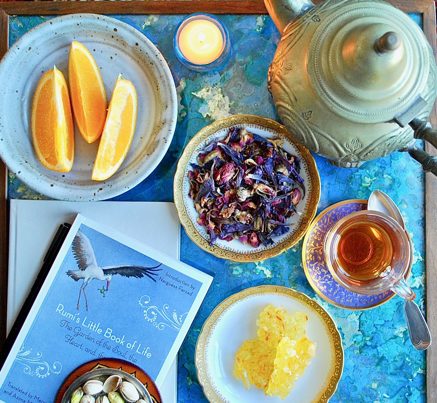 Tea setup featuring a kettle, lemons, sugar, loose tea featuring rose petals, and pistachios on a tray