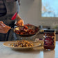 Person preparing a dish with a jar of pomegranate walnut simmer sauce on a kitchen counter.