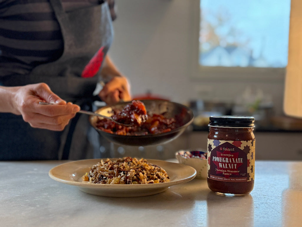 Person preparing a dish with a jar of pomegranate walnut simmer sauce on a kitchen counter.
