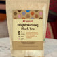 Bag of 'Bright Morning Black Tea' with a small bowl of tea leaves on a wooden surface.